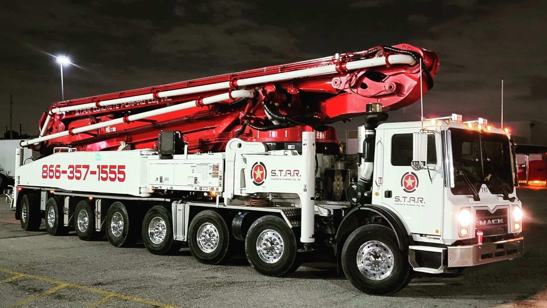 Camión Mack rojo y blanco de bomba pluma de S.T.A.R. Concrete Pumping, iluminado de noche